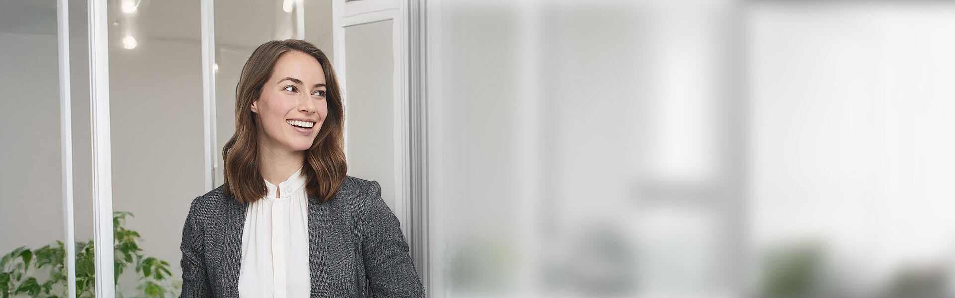 Frau im Büro, professionell gekleidet, vor Glaswänden.